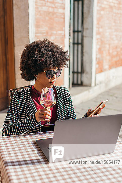 Freiberufliche junge Frau  die ein Smartphone benutzt und einen Wein trinkt