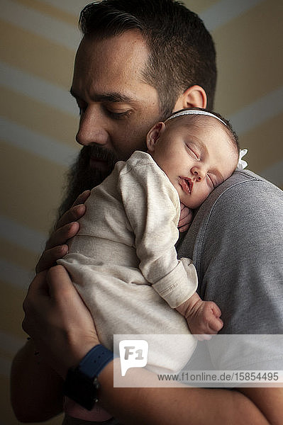 Neugeborenes Mädchen schläft zu Hause bei weichem Licht auf der Schulter des Vaters