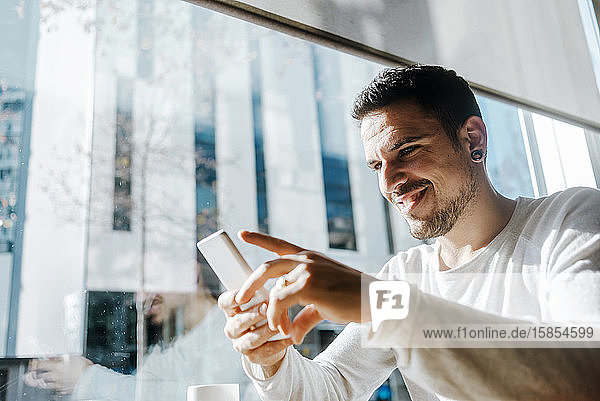 Lächelnder junger Mann  der in einem Café arbeitet und auf sein Handy schaut