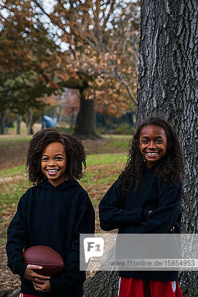 Portrait of smiling sisters with American football in park