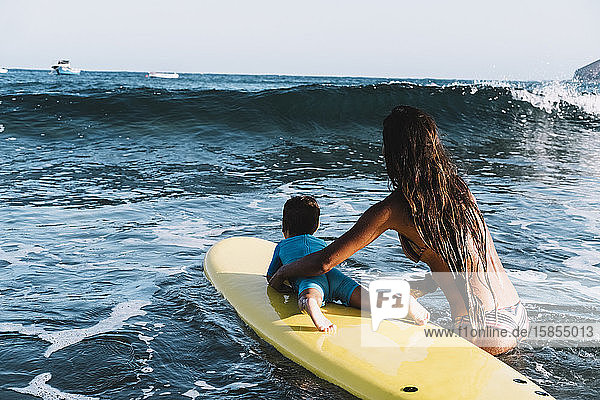 Rückenansicht von Mutter und Sohn auf einem Surfbrett auf See