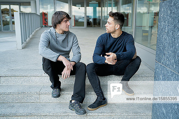 Frontansicht von zwei jungen Männern  die sich auf einer Stadttreppe sitzend unterhalten