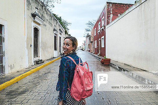 Fröhlicher Reisender mit rosa Rucksack lächelt auf regnerischen Straßen