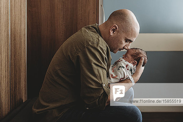 Seitenansicht eines glücklichen Vaters  der seinen neugeborenen Sohn im Krankenhaus umarmt