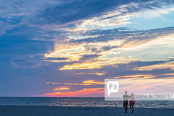 Junges Paar geht am Strand spazieren und bewundert einen wunderschönen Sonnenuntergang.