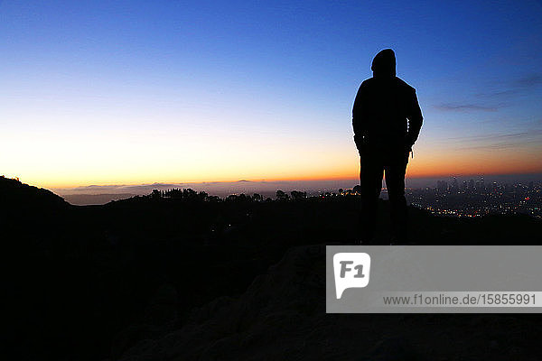 Silhouette eines Mannes  der bei Sonnenaufgang auf der Bergspitze über Los Angeles steht