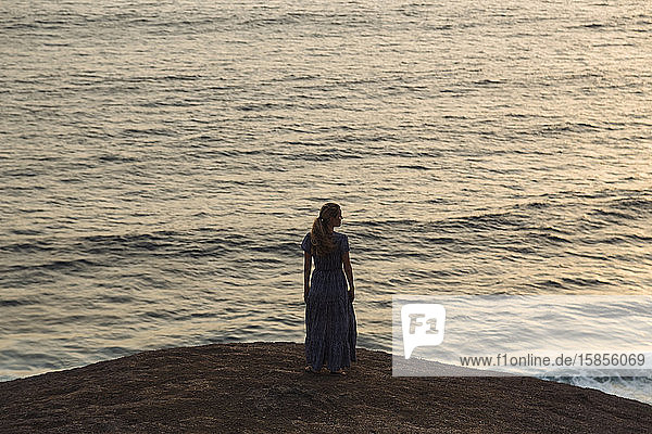 Junge Frau steht bei Sonnenuntergang am Meer