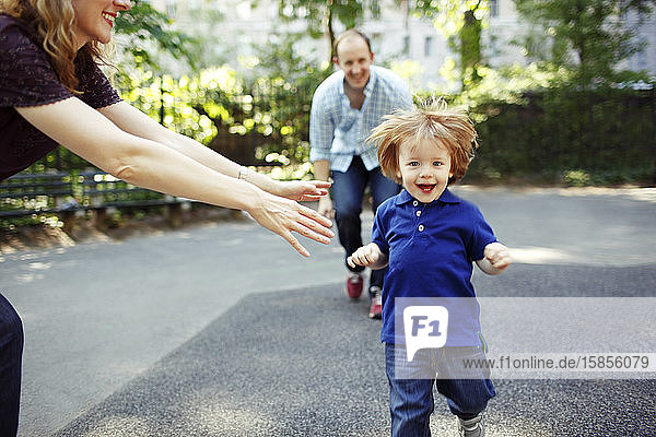 Boy running towards camera as parents playfully chase him