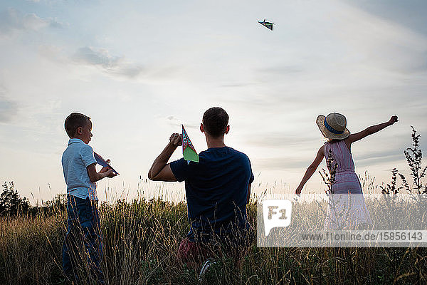 Vater spielt mit seinem Sohn und seiner Tochter bei Sonnenuntergang Papierflieger