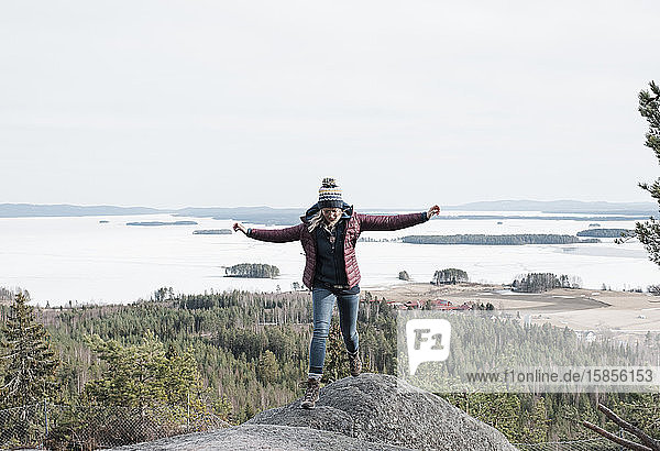 Frau springt über Felsen  während sie in Schweden einen Berg hinaufwandert