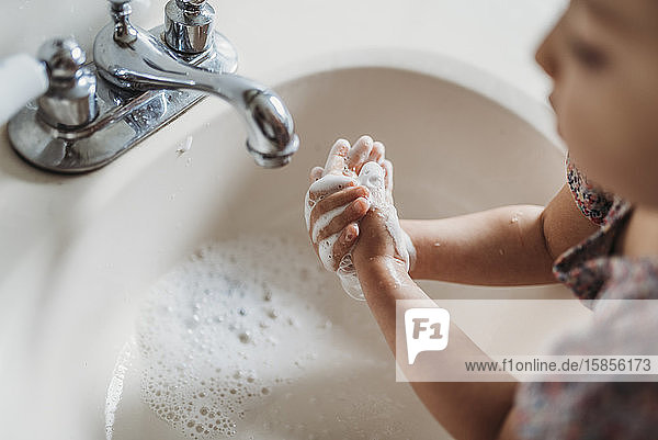 Schrägansicht eines jungen Mädchens  das sich im Waschbecken mit Seife die Hände wäscht