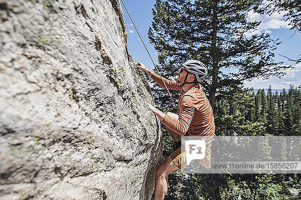 Mann hält sich mit den Fingerspitzen am Fels fest  während er mit einem Seil klettert