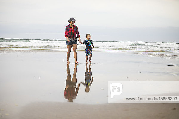eine Mutter  die am Strand spazieren geht und mit ihrem Sohn Händchen hält.