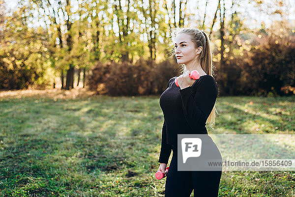 Athletic girl doing fitness outdoors with dumbbells  side view.
