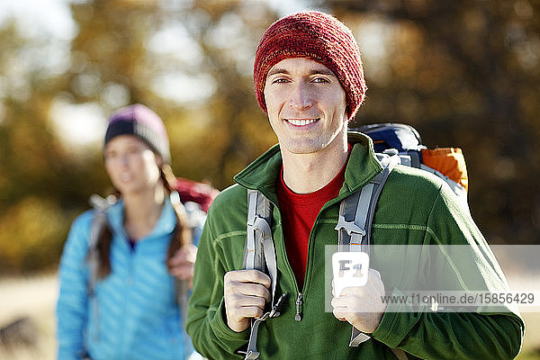Male backpacker looking at camera with female backpacker in background