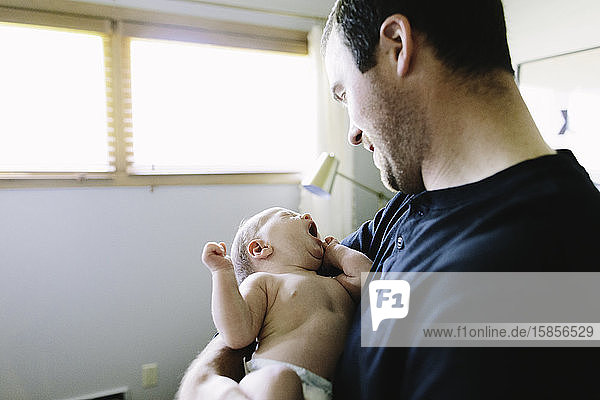 Ein neuer Papa hält seinen neugeborenen Sohn  während er gähnt