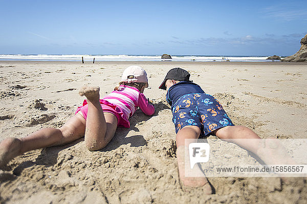Geschwister  die sich in den Sand legen und den Ozean beobachten.