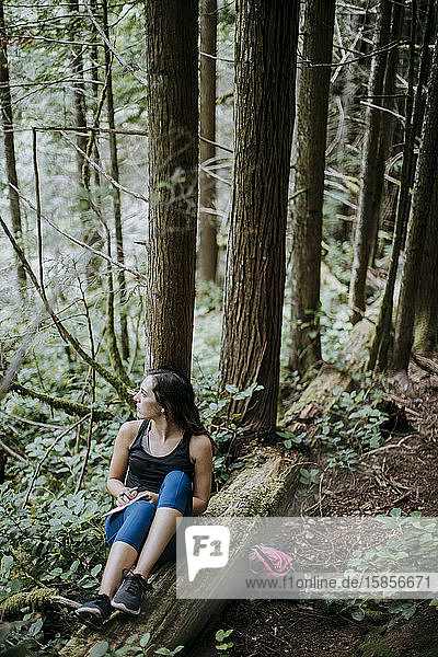 Eine Frau schreibt in einer Zeitschrift  während sie in einem Wald in Washington wandert