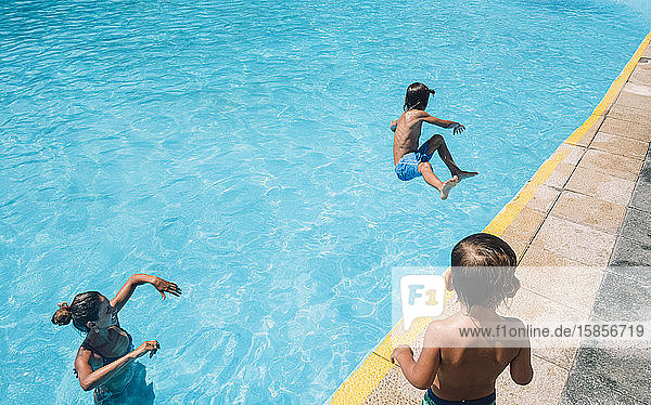 Eine Frau und ein Kind sehen einen Jungen an  der in einen Pool springt