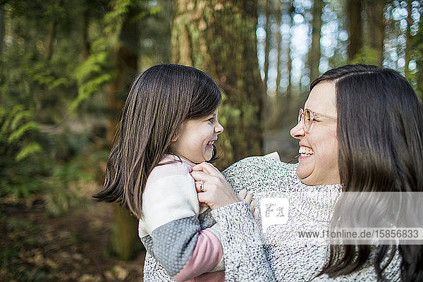 Mother tickling her daughter in outdoor setting.
