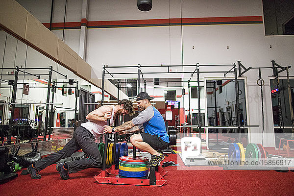 Personal Trainer erhöht das Gewicht auf dem Schlitten der Kunden im Fitnessstudio.