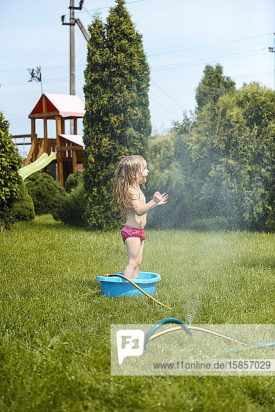Kleines Mädchen spielt zu Hause im Garten mit Wasser