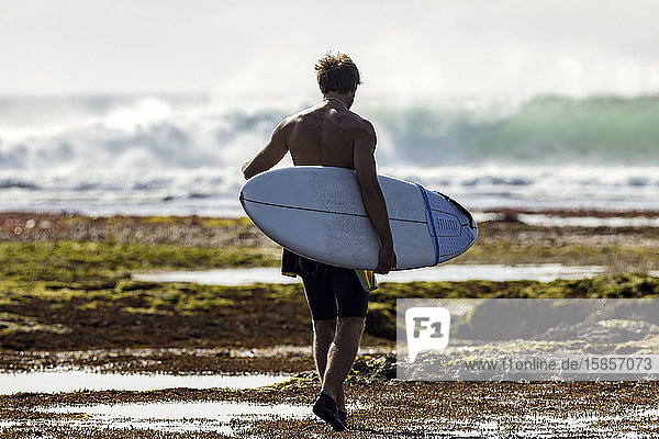 Mann mit Surfbrett beim Spaziergang am Strand