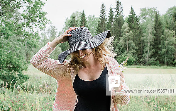 Frau rennt durch ein Feld und hält ihren Hut lächelnd