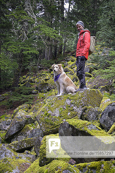 Male hiker and fluffy dog standing on mossy rocks in the mountains
