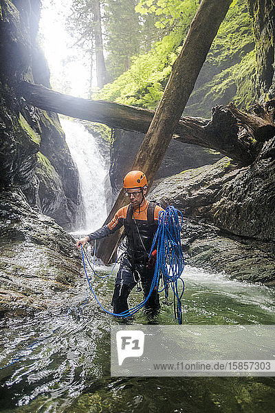 Mann wickelt Seil  nachdem er sich von einem Wasserfall abgeseilt hat.