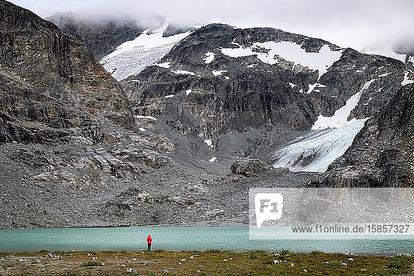 Hiker stands by lake against mountains and glacier