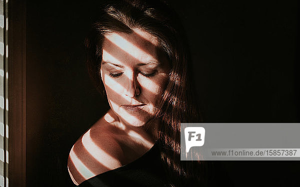 Bildnis einer Frau neben einem Fenster mit Schatten im Gesicht.