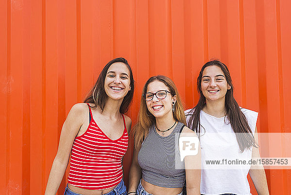 Drei junge glückliche Teenager-Mädchen haben Spaß an oranger Wand