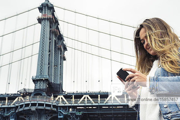 Attraktive Frau benutzt ihr Smartphone auf der Manhattan Bridge