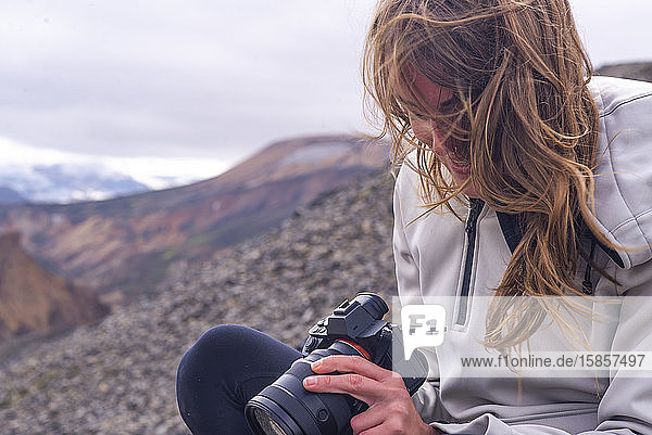 Frau sitzt in Landmannalaugar und schaut in die Kamera in den Wind