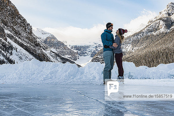 Junges Paar läuft im Winter gemeinsam auf dem zugefrorenen Lake Louise Schlittschuh