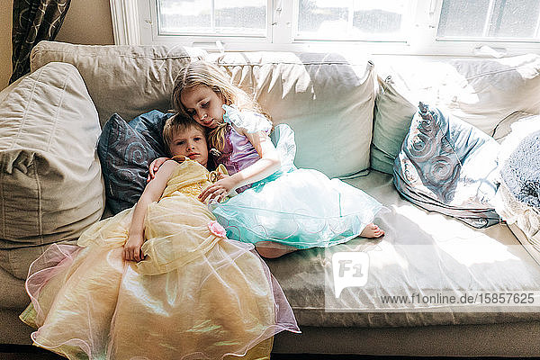 Ein Junge und ein Mädchen in Prinzessinnenkleidern sitzen auf einer Couch.