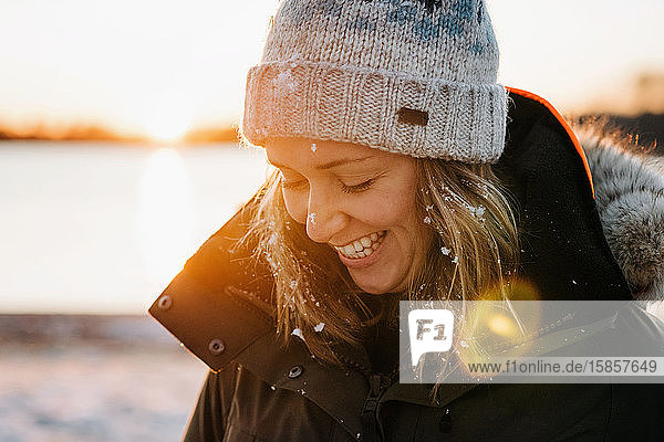 Porträt einer lachenden Frau mit Schnee im Haar im Winter bei Sonnenuntergang