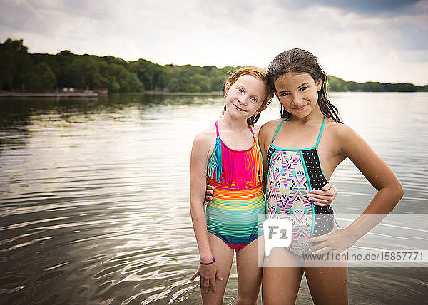 Zwei junge Mädchen in Badeanzügen stehen an einem See