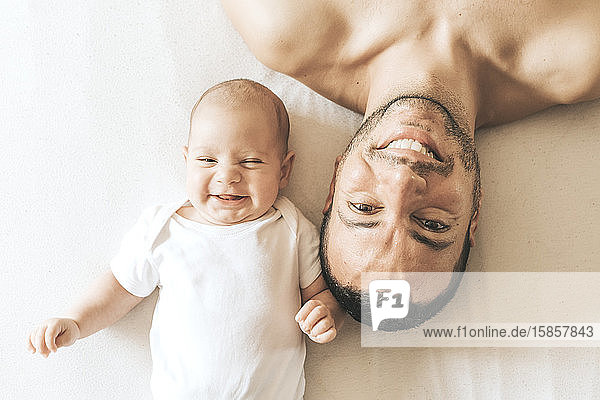 Vater und neugeborener Sohn liegen lachend ausgestreckt im Bett