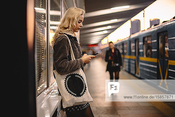 Junge Frau benutzt Smartphone  während sie an der U-Bahn-Station steht