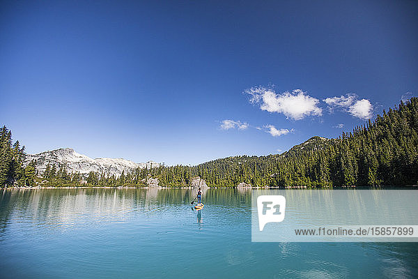 Fitte Frau paddelt stehendes Paddelbrett auf blauem See.