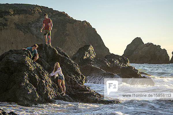 Gruppe von Teenagern  die auf Felsen am Strand herumhängen