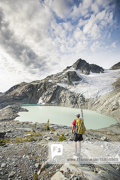 Backpacker stops to look at view of mountains glacier and lake.