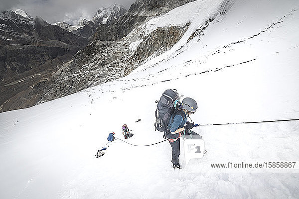 A woman climber ascends a fixed line on a steep snow slope