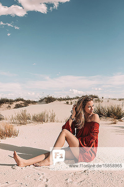 Frau  die auf dem Wüstensand sitzt und über ihre Schulter schaut