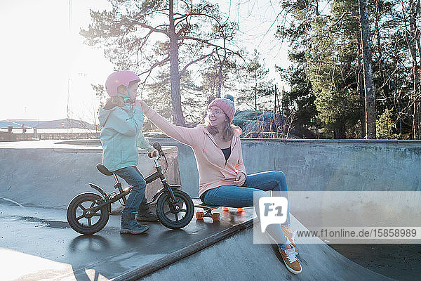 Mutter hilft ihrer Tochter mit ihrem Helm in einem Skatepark