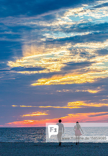 Young couple walking toward ocean during colorful sunset.