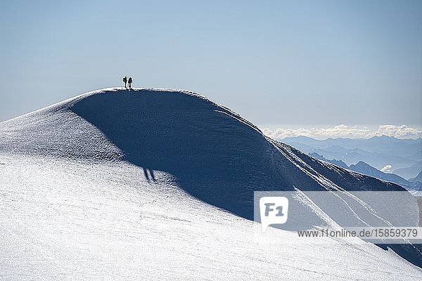 Zwei Bergsteiger stehen als Silhouette auf dem Kamm eines Gletschers auf dem Mt. Baker