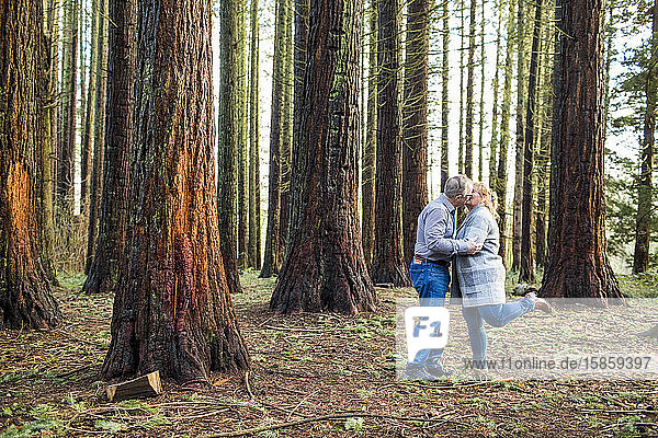 Retired couple kiss romantically in forest.